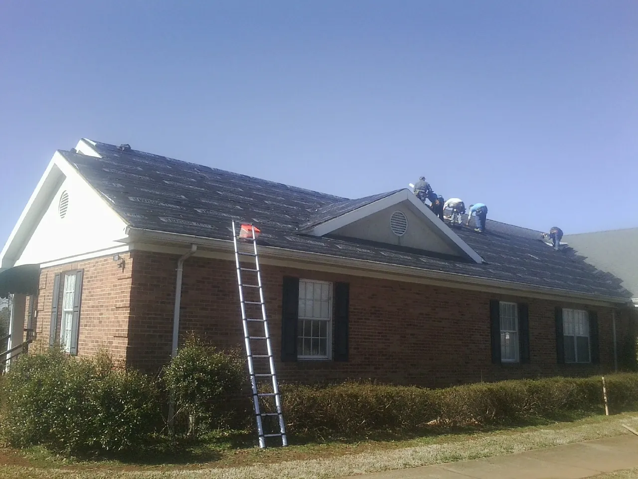 Crew tearing shingles off a brick ranch roof with a ladder set — Metal Roof Repair work by our crew in Biglerville