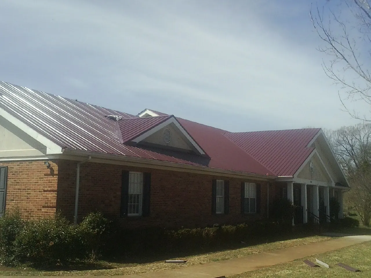 Red metal roof with gabled entries on a long brick building, from a Hail Damage Roof Repair job in Biglerville
