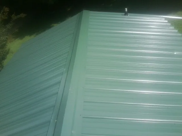 New green metal panels meeting at the ridge of a roof — Flat Roof Repair work by our crew in Biglerville