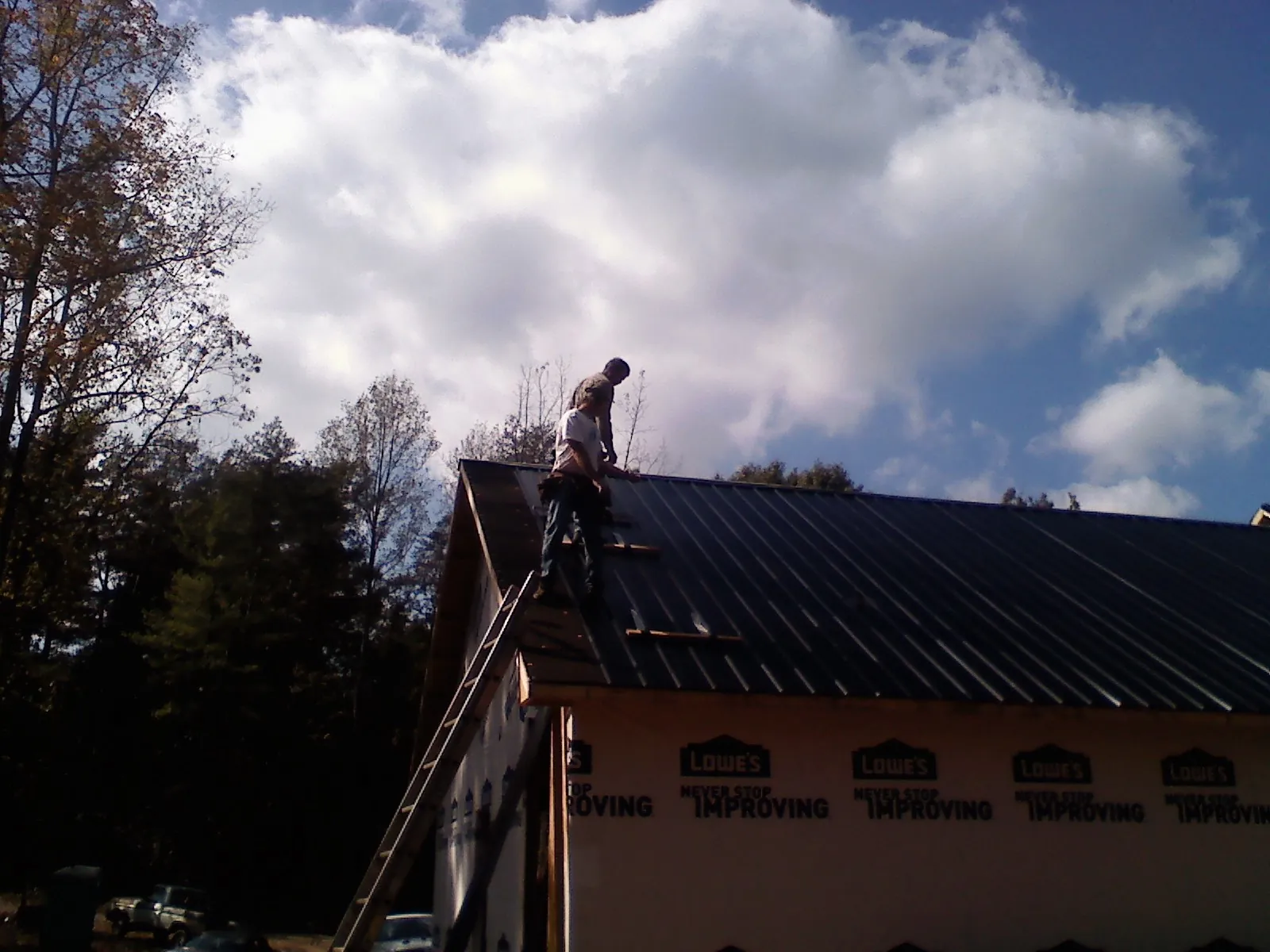 Roofer fastening dark metal panels high against a cloudy sky, from a Roof Inspection job in Biglerville