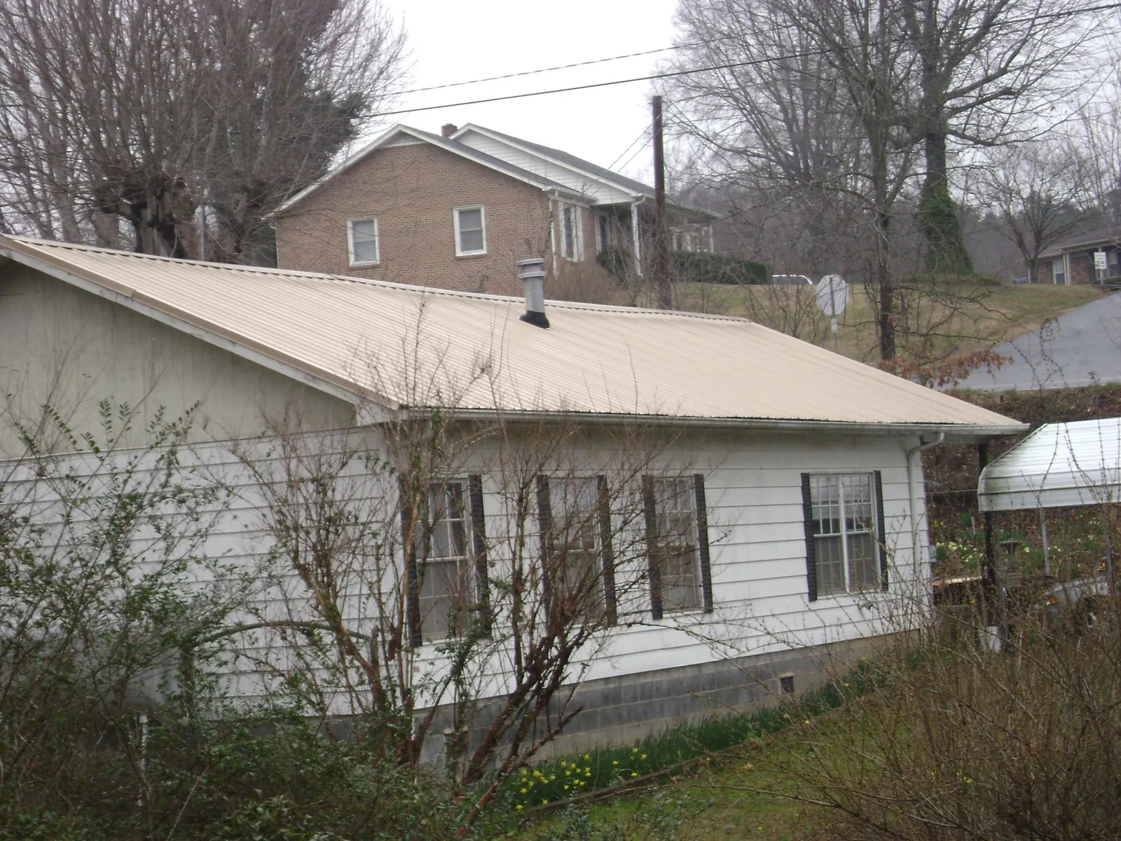Tan metal roof on a white sided house set into a hillside — Commercial Roofing by Roofing Brothers in Biglerville